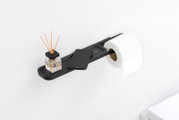 Schwarzer Toilettenpapierhalter mit Ablage, darauf ein Duftstäbchen-Glas und ein Smartphone, seitliche Perspektive