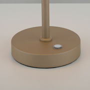 Nahaufnahme der Basis einer goldfarbenen Akku-Tischleuchte mit einem Knopf, seitliche Perspektive.