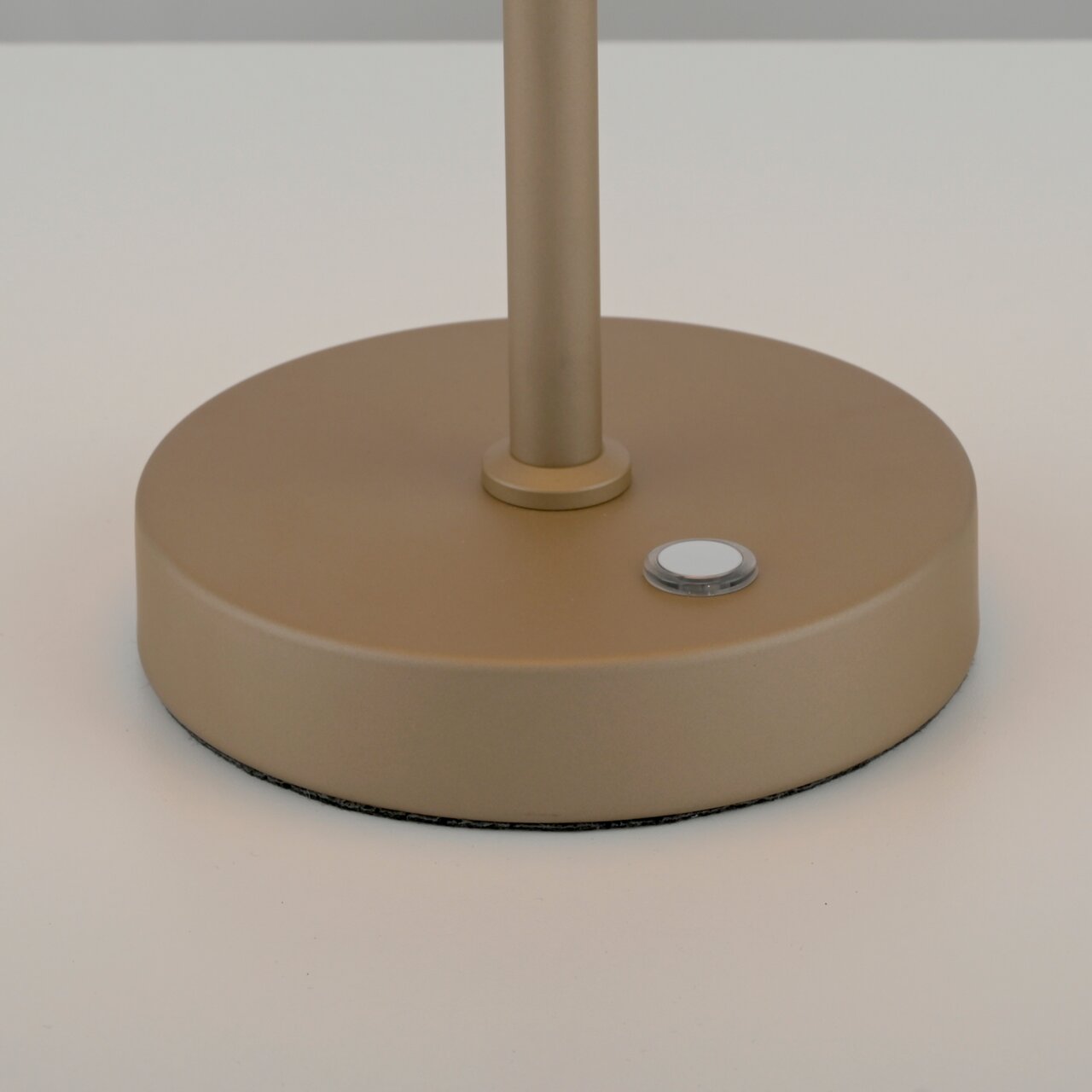 Nahaufnahme der Basis einer goldfarbenen Akku-Tischleuchte mit einem Knopf, seitliche Perspektive.