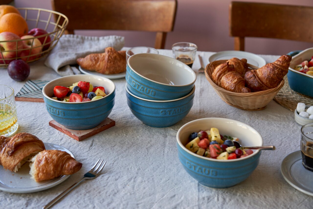 Frühstückstisch mit türkisfarbenem Schüsselset, gefüllt mit frischem Obstsalat, aus seitlicher Perspektive.