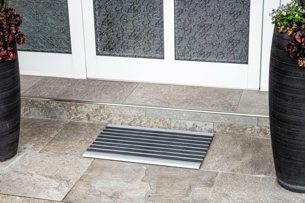 Fußmatte in Streifendesign vor einer Haustür, fotografiert aus der Vogelperspektive.