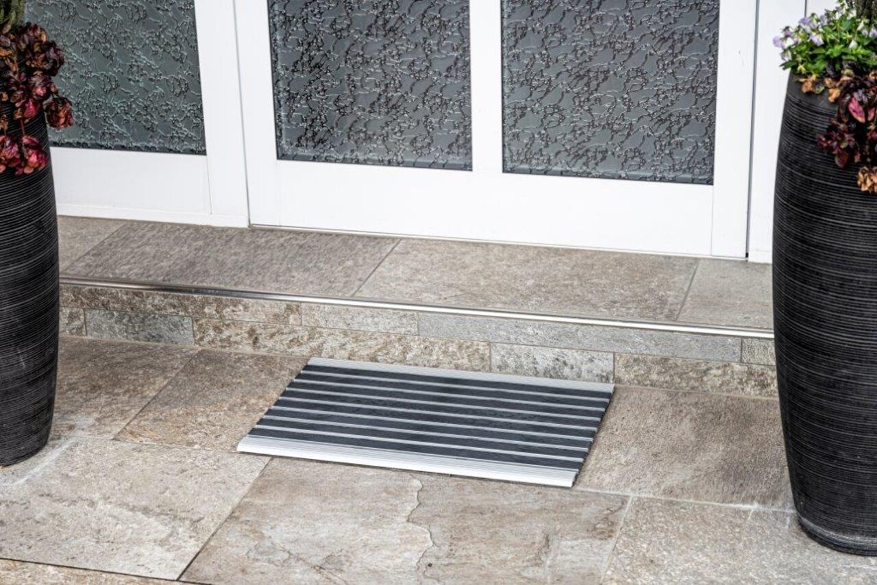 Fußmatte in Streifendesign vor einer Haustür, fotografiert aus der Vogelperspektive.