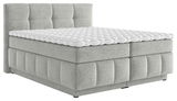 Graues Boxspringbett mit gepolstertem Kopfteil und weißem Topper, seitliche Perspektive