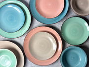 Vogelperspektive auf ein 16-teiliges Kombiservice in Pastellfarben, bestehend aus Tellern und Schalen in Blau, Grün, Rosa und Beige.