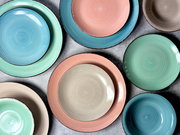 Vogelperspektive auf ein 16-teiliges Kombiservice in Pastellfarben, bestehend aus Tellern und Schalen in Blau, Grün, Rosa und Beige.