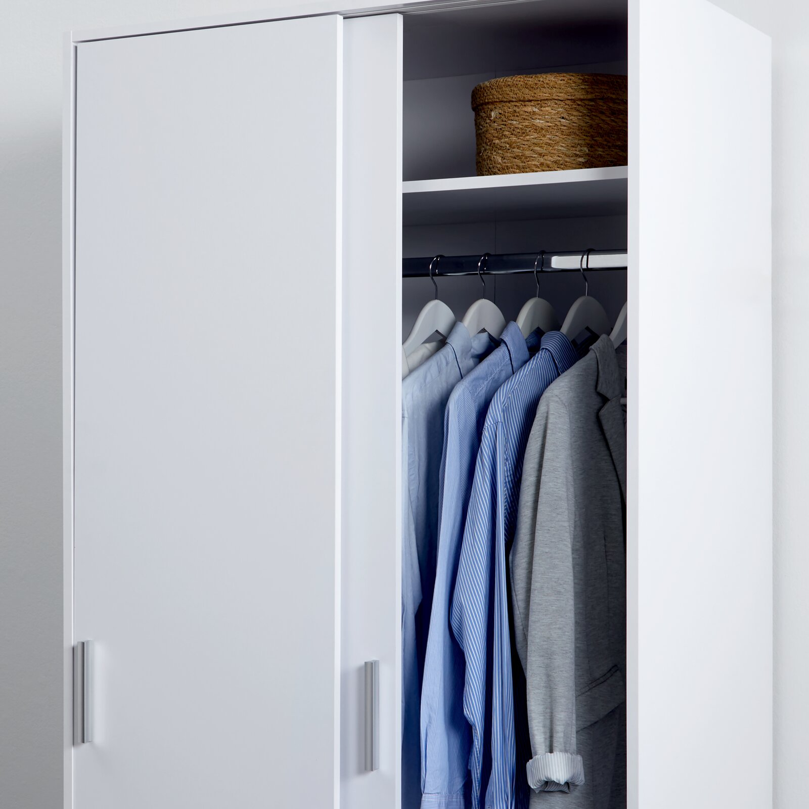 Weißer zweitüriger Schiebetürenschrank XORA MIKA, teilweise geöffnet, mit Kleidung und Korb, seitliche Perspektive
