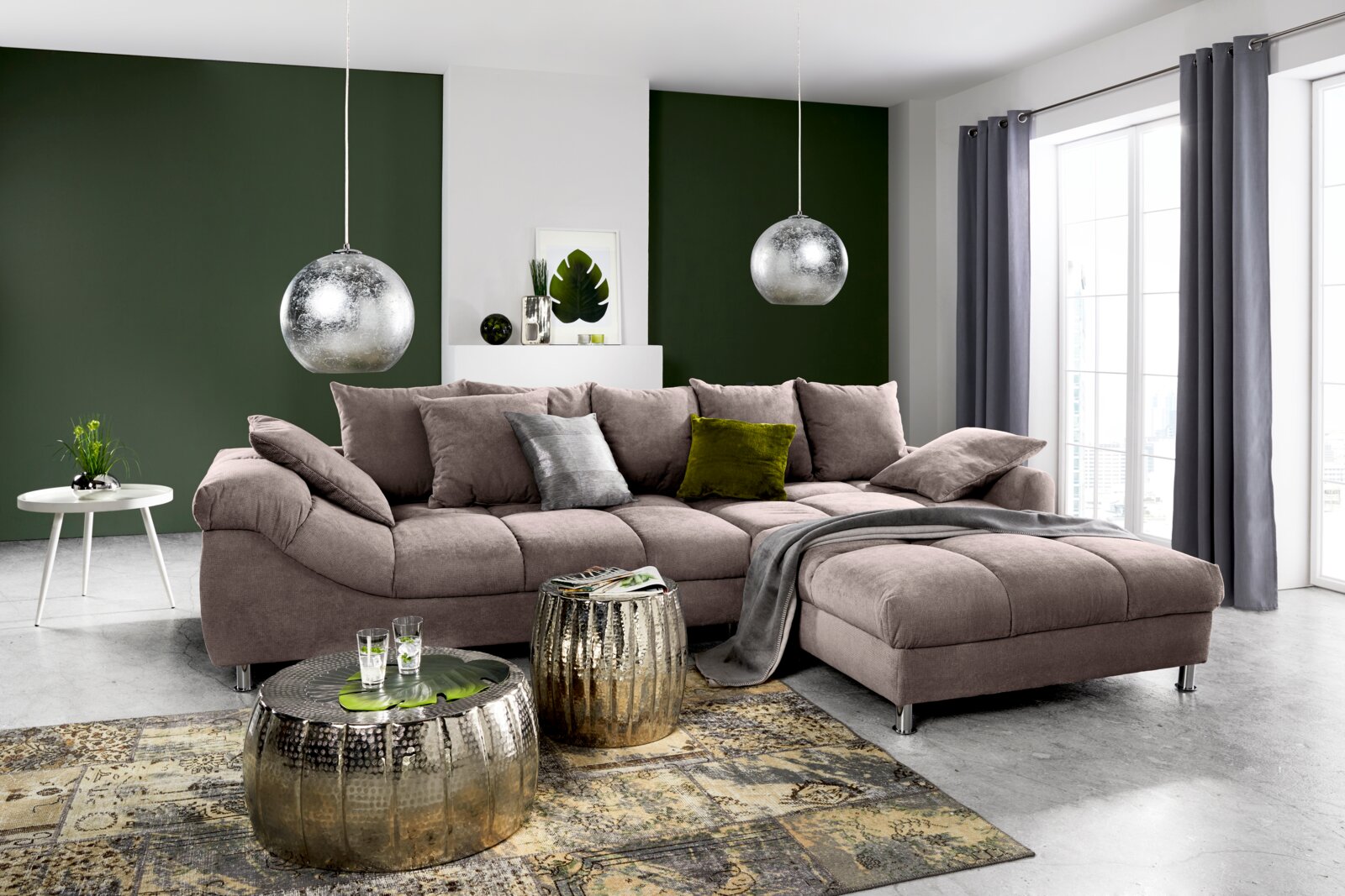 Großes, modernes Ecksofa in einem hellen Wohnzimmer mit grüner Akzentwand, von vorne betrachtet.