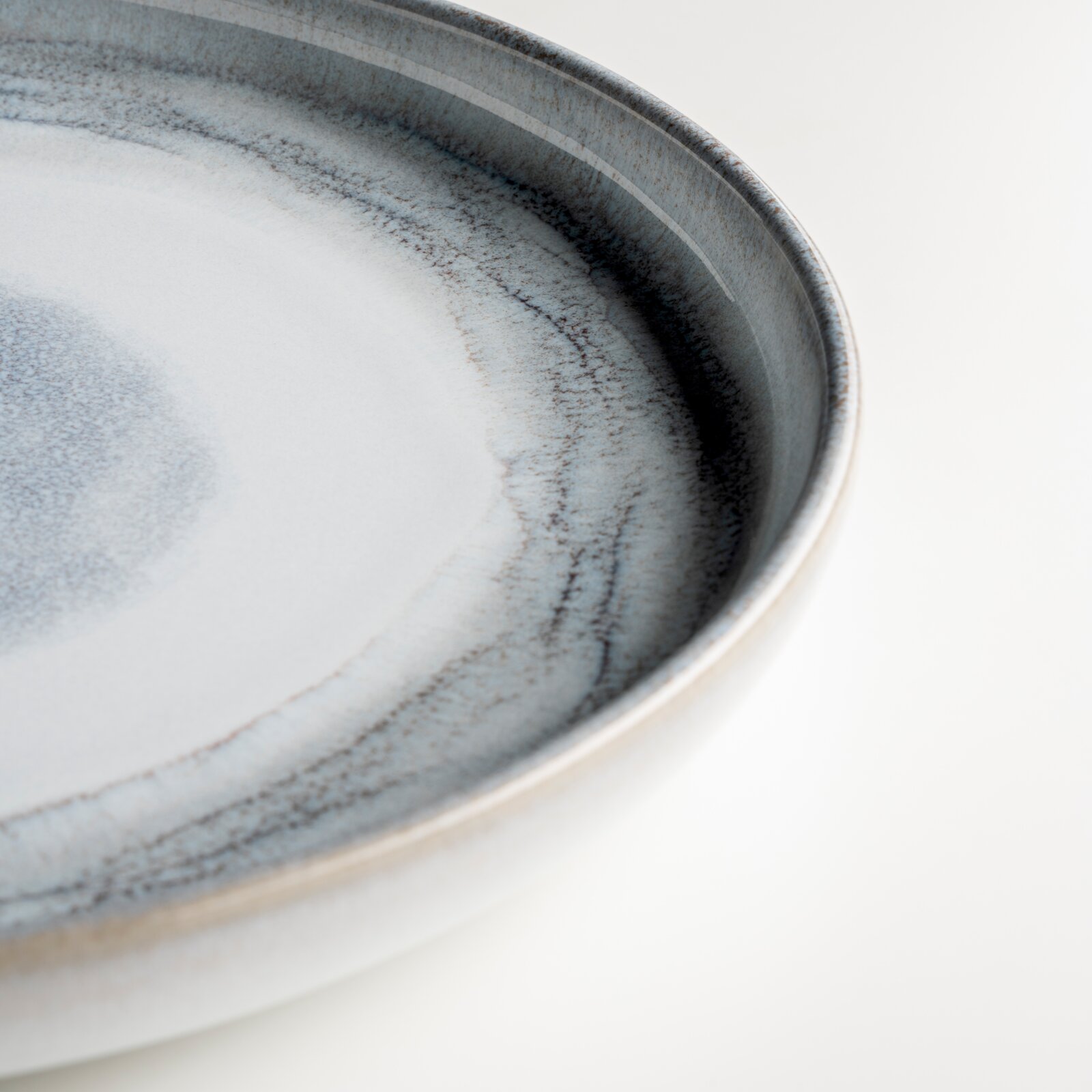 Gipfelstück Tafelservice 12-tlg. TIEFER SEE Nahaufnahme eines runden Keramiktellers in Blau-Grau mit gesprenkelter Glasur und dunklem Rand, schräg von oben fotografiert.