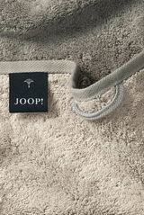 Nahaufnahme eines beigen Gästetuchs mit einer schwarzen Etikette mit der Aufschrift 'JOOP!' und einer Schlaufe zum Aufhängen.