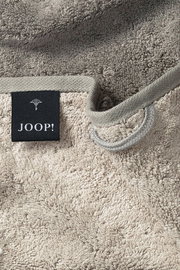 Nahaufnahme eines beigen Gästetuchs mit einer schwarzen Etikette mit der Aufschrift 'JOOP!' und einer Schlaufe zum Aufhängen.