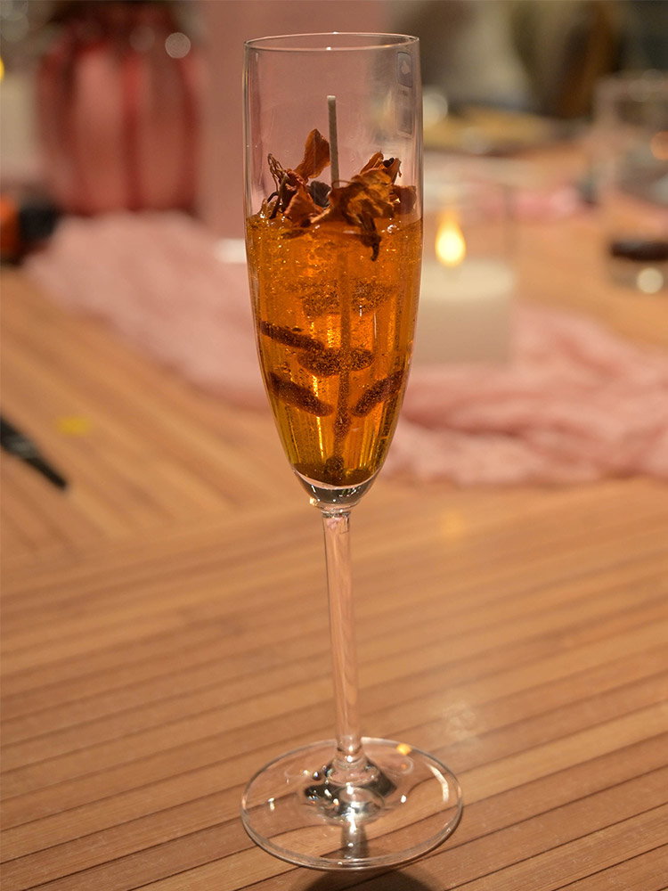 Goudkleurige kaars in een elegant champagneglas, afgewerkt met decoratieve bloemelementen.