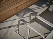 Nahaufnahme eines Stapelsessels mit hellem Metallrahmen und Textilbespannung, neben einem Holztisch, aus der Vogelperspektive fotografiert.