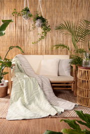 Gemütliche Wohndecke mit Blattmuster in einem natürlichen, tropischen Ambiente, drapiert über einem Sofa. Perspektive von vorne.