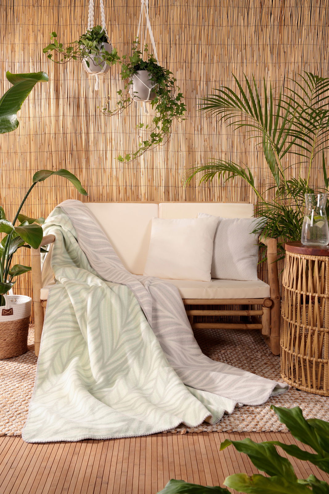 Gemütliche Wohndecke mit Blattmuster in einem natürlichen, tropischen Ambiente, drapiert über einem Sofa. Perspektive von vorne.