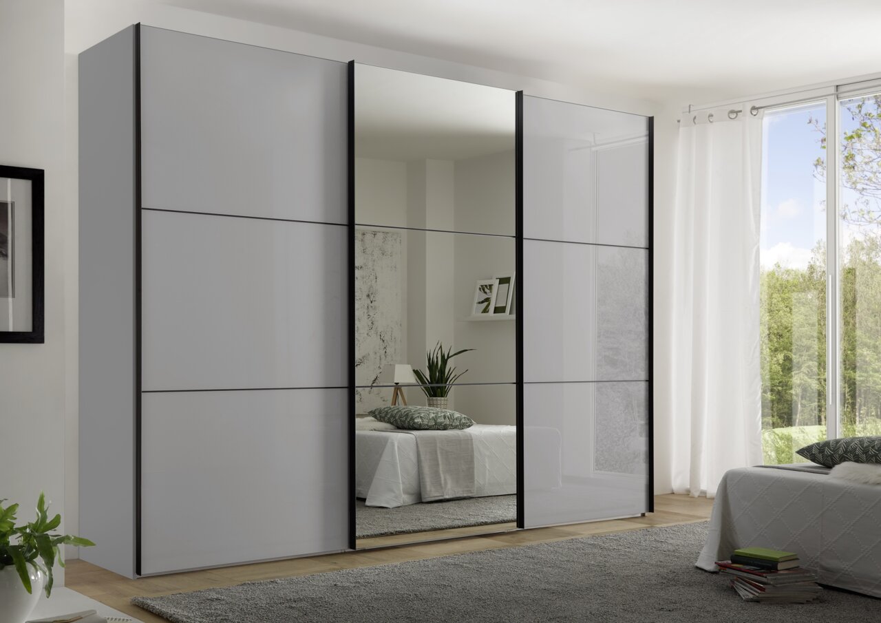 Moderano Schwebetürenschrank PRIMO Moderano Schwebetürenschrank PRIMO in einem modernen Schlafzimmer, frontal betrachtet, mit einem großen Spiegel in der Mitte und eleganten, grauen Türen.