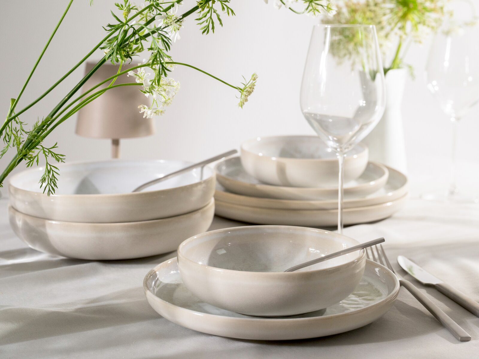 Elegantes cremefarbenes Keramikgeschirr mit Tellern und Schalen auf einer festlich gedeckten Tafel, aus leicht erhöhter frontaler Perspektive inszeniert