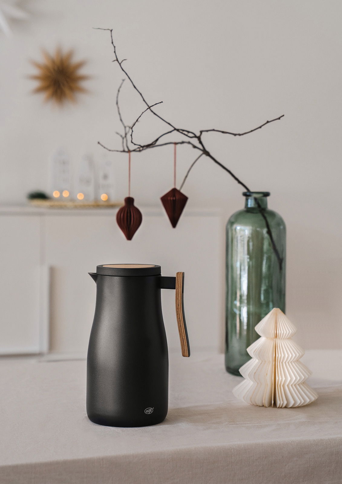 Schwarze Isolierkanne Studio Allure mit Holzgriff, seitliche Perspektive, auf einem Tisch mit dekorativen Elementen im Hintergrund.