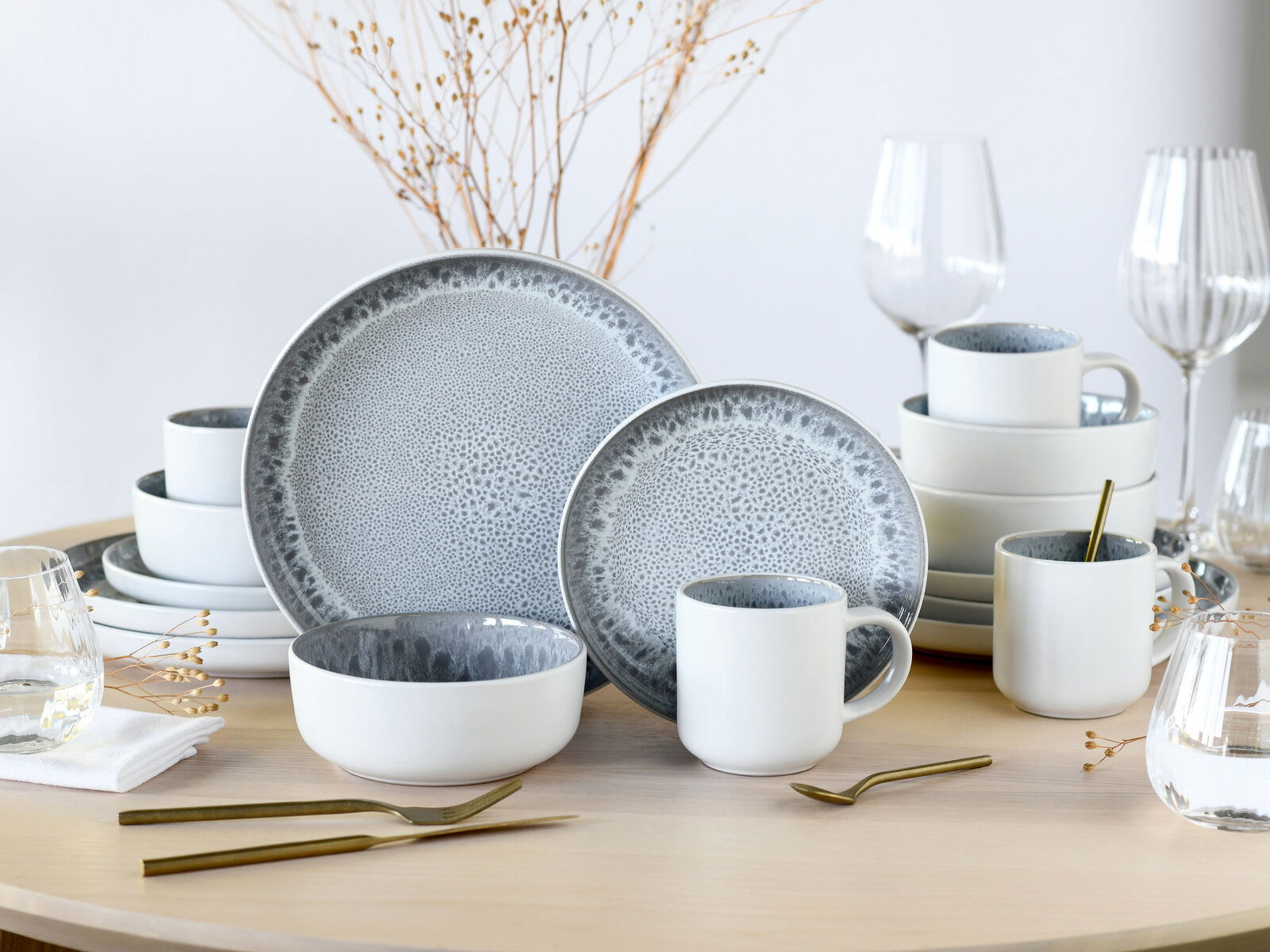 Kombiservice 16-tlg. Stone auf einem Tisch arrangiert, mit Tellern, Tassen und Schalen in modernem Design, aus seitlicher Perspektive fotografiert.