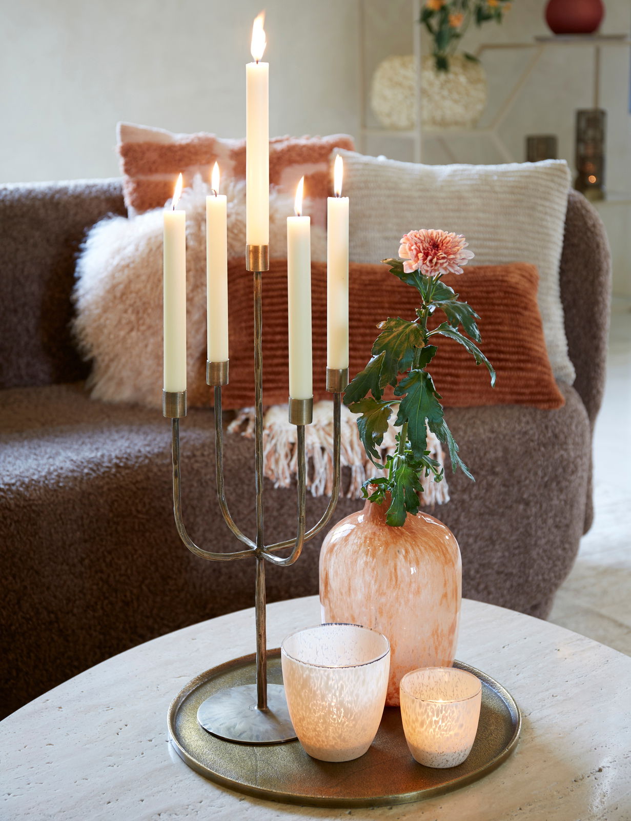 Runde, antike Schale aus Metall mit einem Durchmesser von 40 cm, dekoriert mit einem Kerzenhalter, einer Vase und zwei Teelichthaltern, auf einem Tisch in einem gemütlichen Wohnzimmer arrangiert. Perspektive von oben.