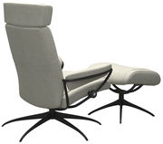 Rückansicht eines modernen Einzelsessels mit Kopfstütze und passendem Fußhocker in hellem Stoffbezug, auf schwarzem Metallgestell.