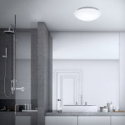 Witte, ronde plafondlamp in een moderne badkamer, gezien van onderaf (plafondaanzicht) met douchewand en wastafel op de achtergrond