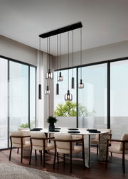 Moderne Pendelleuchte über einem Esstisch in einem eleganten, lichtdurchfluteten Raum mit großen Fenstern, seitliche Perspektive.