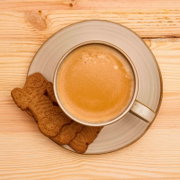 Tasse Kaffee mit Crema auf Untertasse neben zwei Spekulatius-Keksen auf hellem Holztisch, Draufsicht von oben