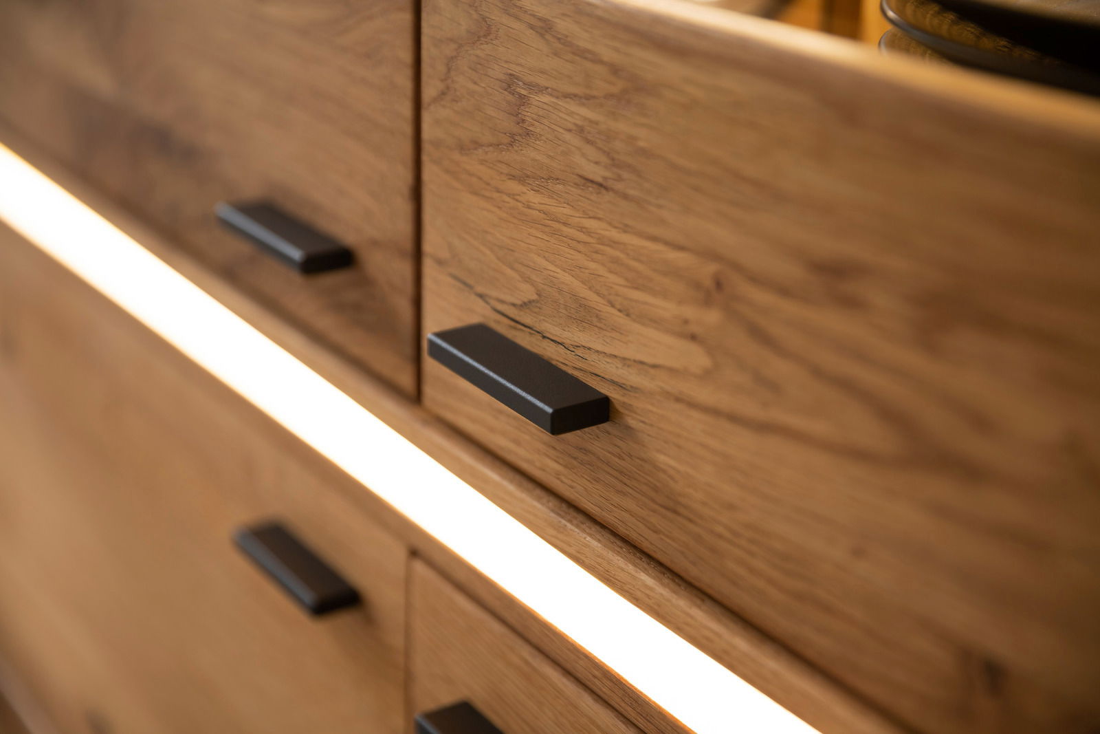 Nahaufnahme eines Highboards aus Holz mit modernen schwarzen Griffen und integrierter Beleuchtung, seitliche Perspektive