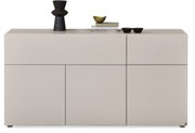 Frontansicht eines modernen, grifflosen Sideboards in hellem Beige mit geometrisch unterteilten Türen und dekorativen Schalen sowie einer schwarzen Vase auf der Oberseite.