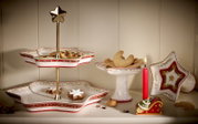 Festliches Weihnachtsgeschirr in Sternform mit rot-grünen Ornamenten, präsentiert in leichter Frontalansicht von oben mit Plätzchen, Etagere und brennender Kerze