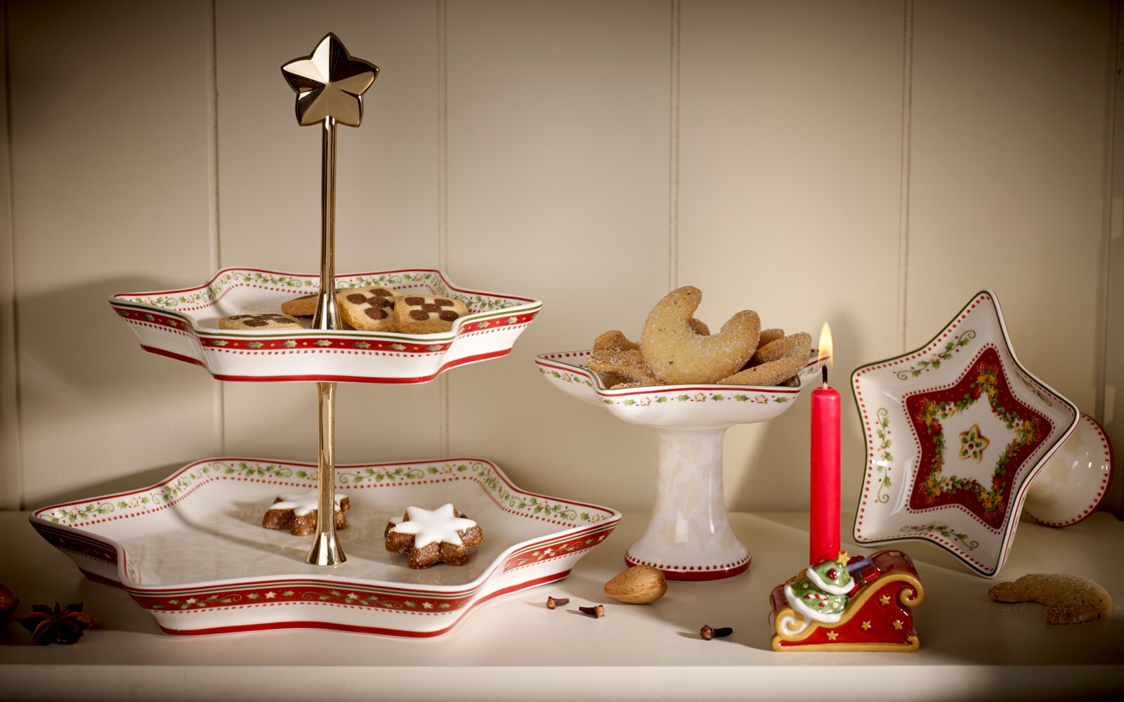 Festliches Weihnachtsgeschirr in Sternform mit rot-grünen Ornamenten, präsentiert in leichter Frontalansicht von oben mit Plätzchen, Etagere und brennender Kerze