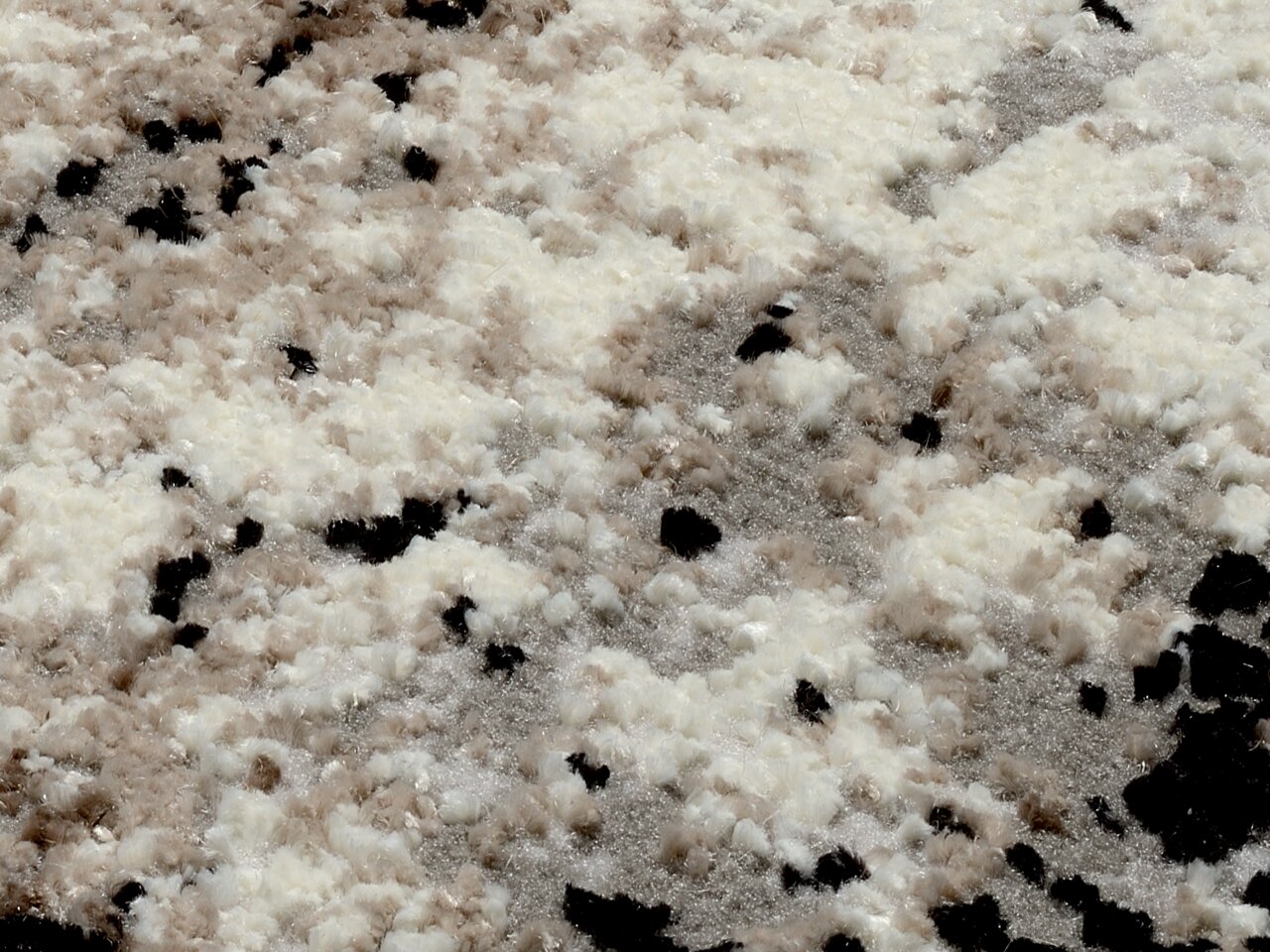 Nahaufnahme eines Designer Teppichs mit flauschiger Textur in Creme-, Beige- und Schwarztönen, aus der Vogelperspektive aufgenommen.