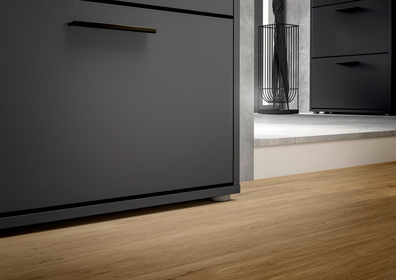 Nahaufnahme eines modernen, schwarzen Schuhkippers mit Metallgriff, auf Holzfußboden, seitliche Perspektive.