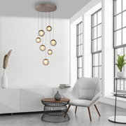 Moderne LED-Pendelleuchte mit mehreren Glaskugeln, hängend von der Decke in einem stilvollen Wohnzimmer mit großen Fenstern, seitliche Perspektive.