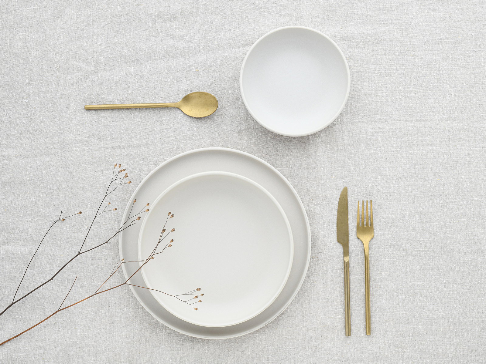 Elegantes 12-teiliges Tellerset in Weiß mit goldfarbenem Besteck, aus der Vogelperspektive auf einem hellen Tischtuch arrangiert.