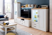 Lichte woonkamer met een witte wandmeubel in landhuisstijl met houten oppervlakken, tv-meubel, vitrinekast met glazen vak en wandplank, gefotografeerd vanuit een licht schuin perspectief