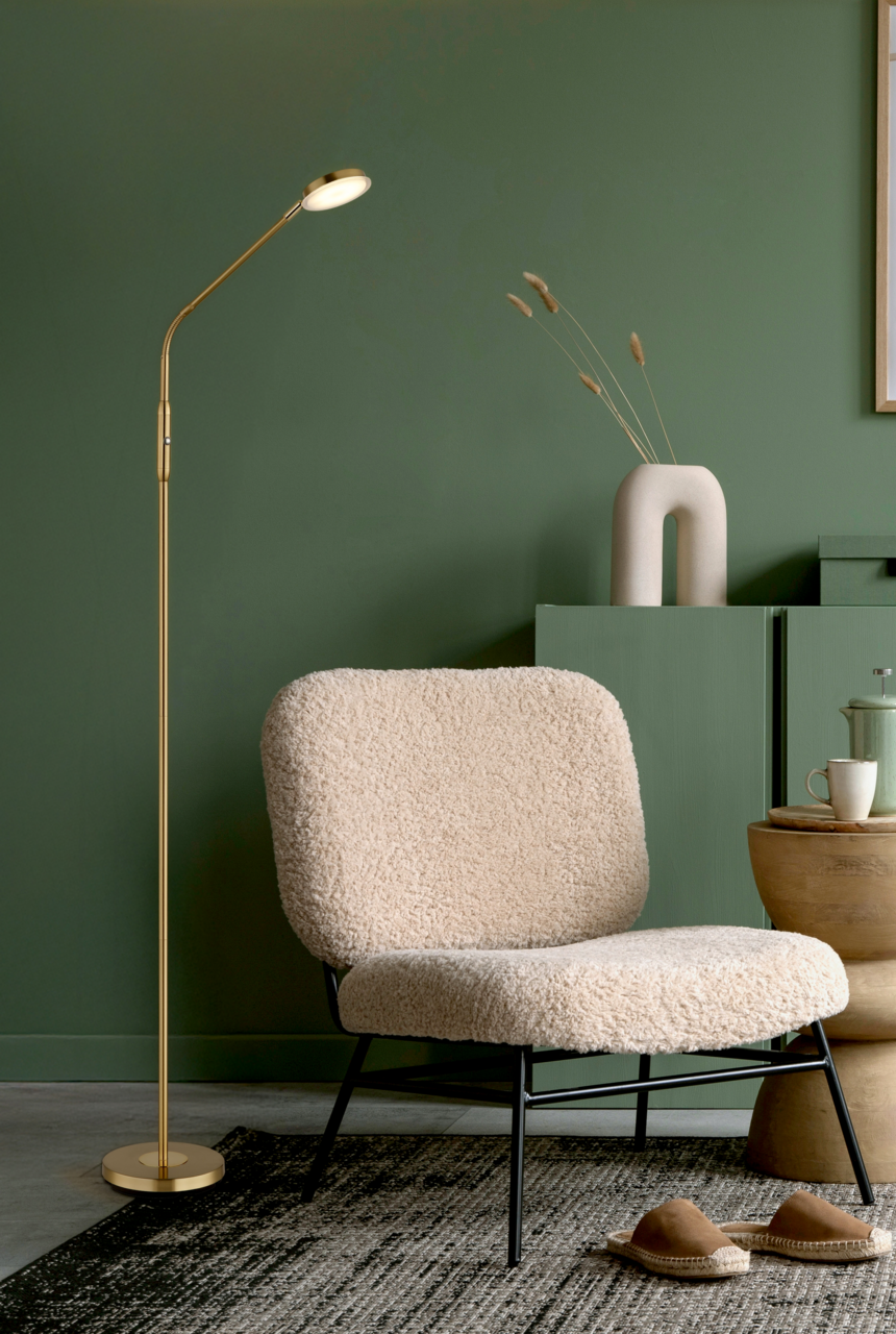 Elegante LED-Stehleuchte in Gold neben einem gemütlichen Sessel in einem stilvoll eingerichteten Raum, seitliche Perspektive