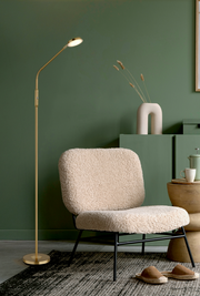 Elegante LED-Stehleuchte in Gold neben einem gemütlichen Sessel in einem stilvoll eingerichteten Raum, seitliche Perspektive