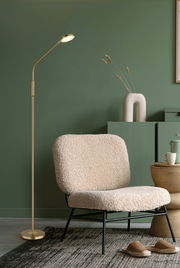 Elegante LED-Stehleuchte in Gold neben einem gemütlichen Sessel in einem stilvoll eingerichteten Raum, seitliche Perspektive
