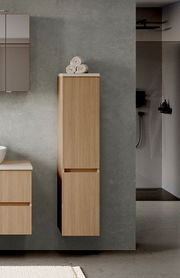 Moderner Midischrank aus Holz in einem Badezimmer, frontal betrachtet, mit Handtüchern obenauf.