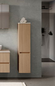 Moderner Midischrank aus Holz in einem Badezimmer, frontal betrachtet, mit Handtüchern obenauf.