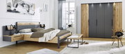 Modernes Schlafzimmer mit einem Holzbett und Nachttischen, einem großen Kleiderschrank und einem Fenster im Hintergrund. Perspektive von der Seite des Bettes.
