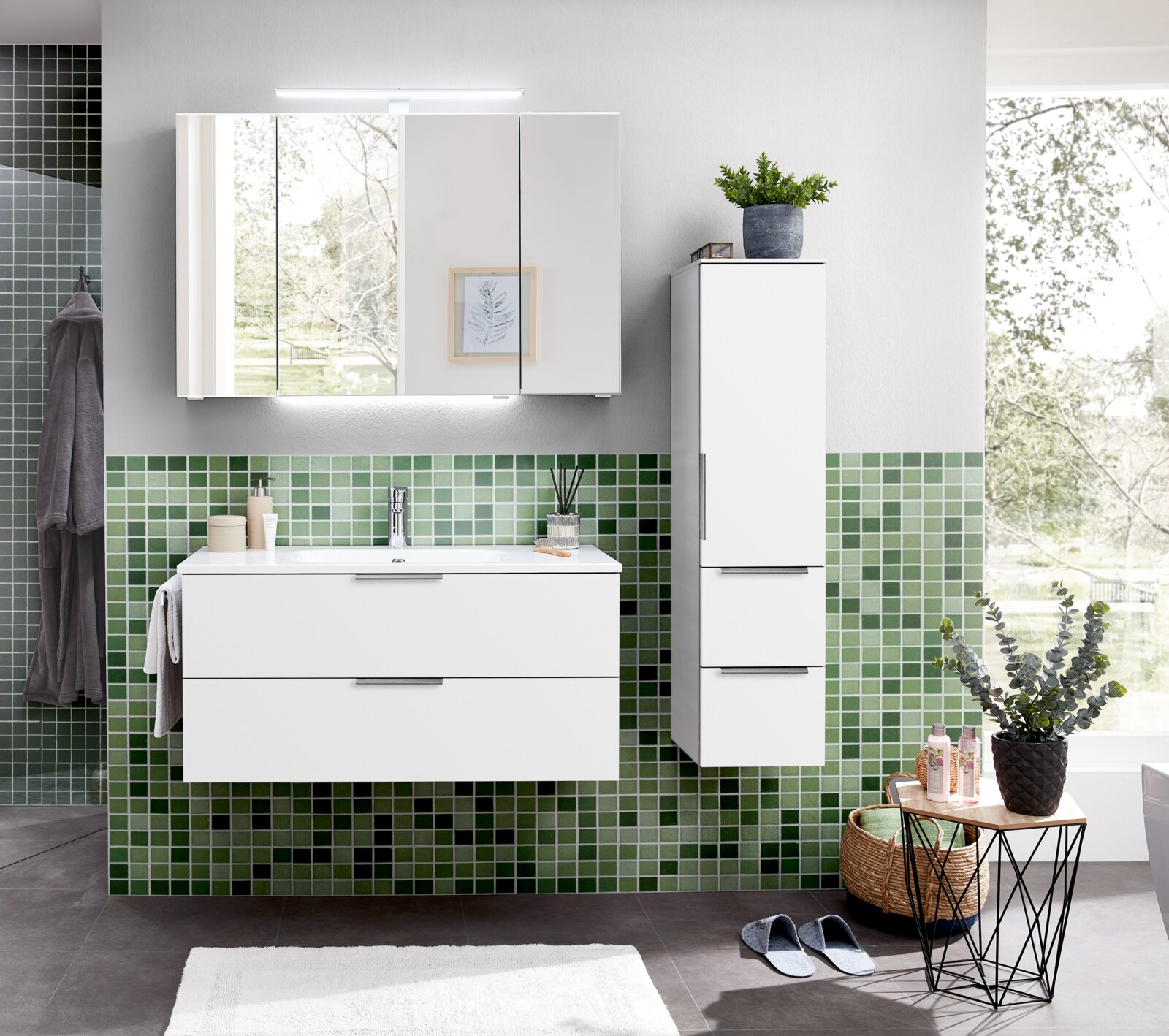 Modernes Badezimmer-Set in Weiß mit Waschtischunterschrank, Spiegel- und Hochschrank vor grüner Mosaikfliesenwand, frontale Ansicht