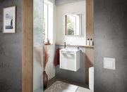 Modernes Gästebad mit weißem Waschbeckenunterschrank, Spiegel und minimalistischer Dekoration, seitliche Perspektive.