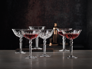 Sechs elegante Cocktailschalen aus Kristallglas mit rotem Getränk, auf einer Tischoberfläche in stilvoller Umgebung, seitliche Perspektive.