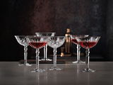 Sechs elegante Cocktailschalen aus Kristallglas mit rotem Getränk, auf einer Tischoberfläche in stilvoller Umgebung, seitliche Perspektive.