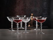 Sechs elegante Cocktailschalen aus Kristallglas mit rotem Getränk, auf einer Tischoberfläche in stilvoller Umgebung, seitliche Perspektive.
