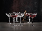 Sechs elegante Cocktailschalen aus Kristallglas mit rotem Getränk, auf einer Tischoberfläche in stilvoller Umgebung, seitliche Perspektive.