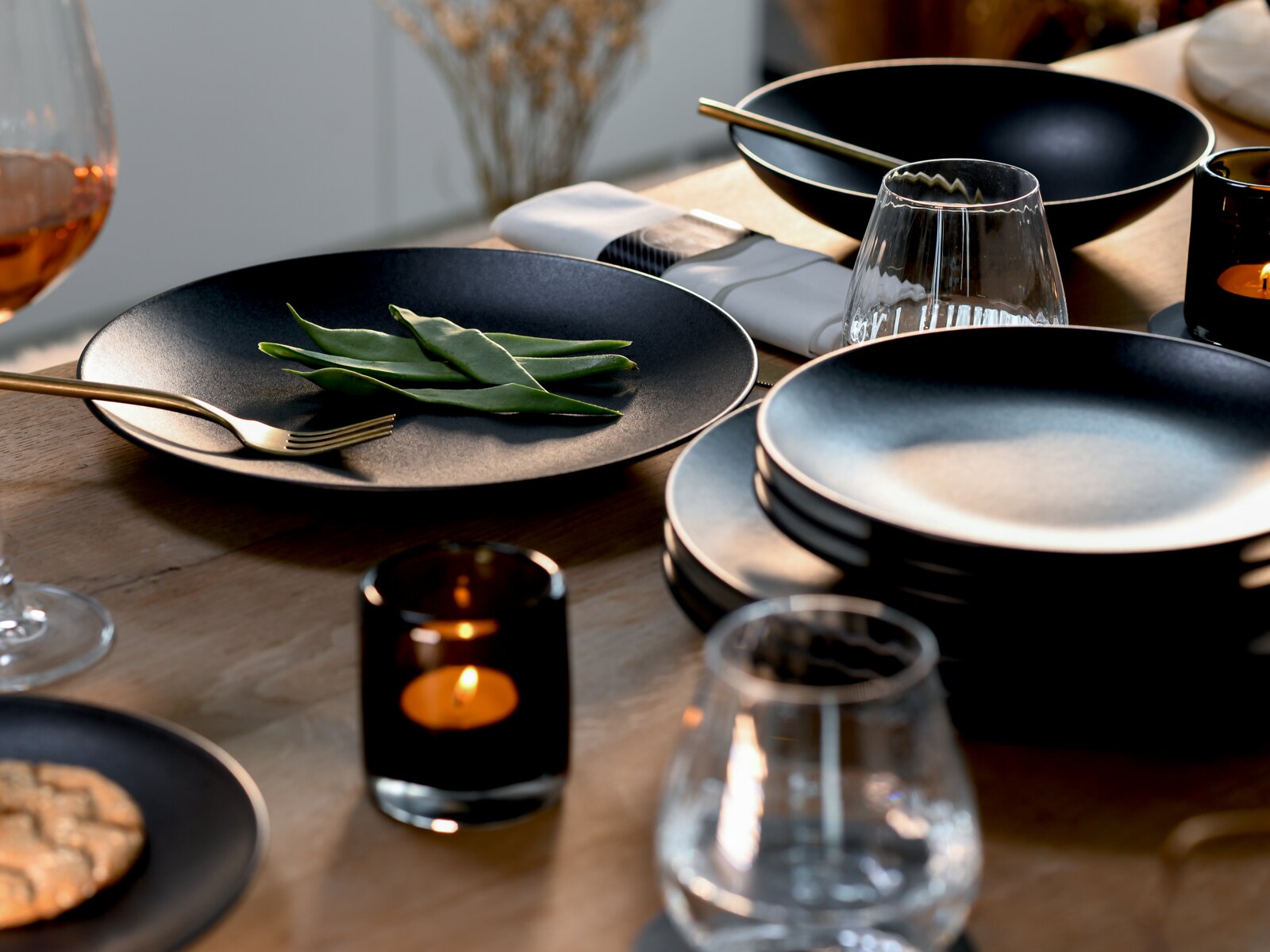 Elegantes schwarzes Geschirrset mit Tellern und Schalen auf einer stilvoll gedeckten Tafel, aus leicht erhöhter Seitenperspektive fotografiert