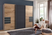 Moderner Schwebetürenschrank mit drei Türen in Holzoptik und grauen Elementen, frontal fotografiert in einem stilvoll eingerichteten Raum.